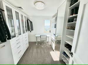 Primary bedroom spacious closet with carpet, custom cabinetry, desk area