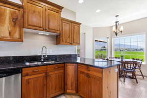 Kitchen with dark stone counters, stainless steel dishwasher, decorative light fixtures, a mountain view, and sink