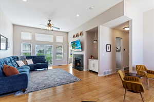 Living room with a tile fireplace, light wood-type flooring, and ceiling fan