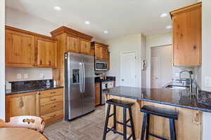 Kitchen with sink, appliances with stainless steel finishes, a kitchen breakfast bar, and dark stone counters