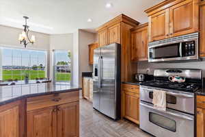 Kitchen with dark stone counters, decorative light fixtures, stainless steel appliances, an inviting chandelier, and light tile patterned floors