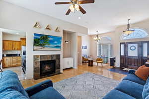 Living room with ceiling fan with notable chandelier, light hardwood / wood-style floors, and a tile fireplace