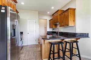 Kitchen with dark stone countertops, light tile patterned floors, kitchen peninsula, a kitchen breakfast bar, and stainless steel fridge