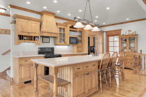 Kitchen featuring a center island with sink, light hardwood / wood-style flooring, black appliances, and custom exhaust hood