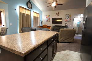 Kitchen with ceiling fan, black fridge, a center island, lofted ceiling, and light tile patterned floors