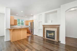 Kitchen featuring kitchen peninsula, dark wood-type flooring, a premium fireplace, high end refrigerator, and sink