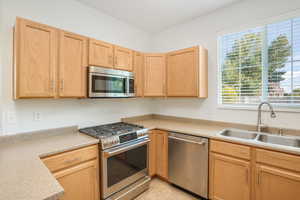 Kitchen with light brown cabinetry, sink, appliances with stainless steel finishes, and light tile patterned floors