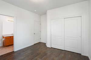 Unfurnished bedroom featuring a closet, ensuite bathroom, and dark hardwood / wood-style floors