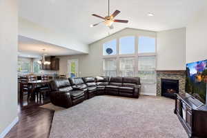 Living room featuring a stone fireplace, dark hardwood / wood-style flooring, ceiling fan with notable chandelier, and lofted ceiling