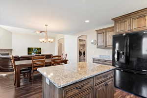 Kitchen with a stone fireplace, ceiling fan with notable chandelier, a center island, dark wood-type flooring, and black fridge