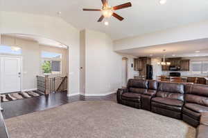 Living room with vaulted ceiling, ceiling fan with notable chandelier, and hardwood / wood-style floors