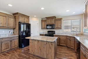 Kitchen with black appliances, sink, light stone countertops, a center island, and dark hardwood / wood-style flooring