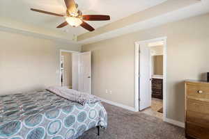 Bedroom with a tray ceiling, connected bathroom, carpet floors, and ceiling fan