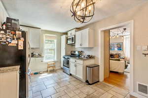 Kitchen with white cabinetry, appliances with stainless steel finishes, light tile patterned floors, and an inviting chandelier