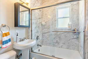 Bathroom featuring toilet and shower / bath combination with glass door