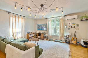 Living room with a wall unit AC, a textured ceiling, and hardwood / wood-style flooring