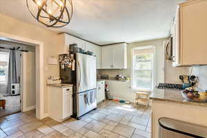 Kitchen featuring a notable chandelier, light stone countertops, appliances with stainless steel finishes, and light tile patterned floors