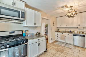 Kitchen with appliances with stainless steel finishes, white cabinets, an inviting chandelier, pendant lighting, and light stone countertops