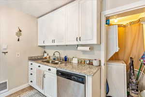 Kitchen with white cabinets, sink, light stone countertops, light tile patterned flooring, and dishwasher