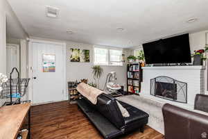 Living room featuring dark wood-type flooring, a textured ceiling, and a brick fireplace