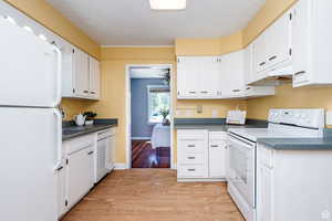 Kitchen with sink, white cabinetry, light wood-type flooring, and white appliances