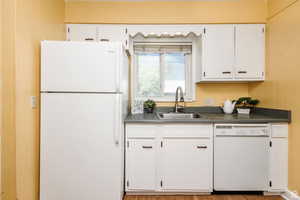 Kitchen with white cabinets, hardwood / wood-style flooring, white appliances, and sink