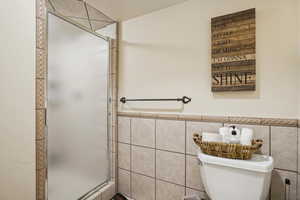 Bathroom featuring toilet, an enclosed shower, and tile walls