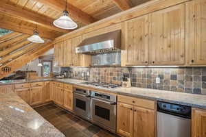 Kitchen with wall chimney range hood, appliances with stainless steel finishes, dark tile patterned flooring, decorative backsplash, and decorative light fixtures