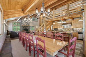 Tiled dining room featuring lofted ceiling with beams, a fireplace, rustic walls, a chandelier, and wooden ceiling