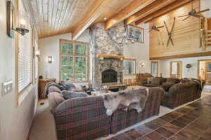 Tiled living room featuring ceiling fan, high vaulted ceiling, beamed ceiling, a stone fireplace, and wood ceiling