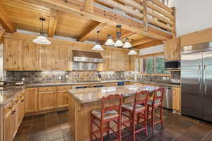 Kitchen featuring a center island, built in appliances, dark tile patterned floors, and wall chimney exhaust hood