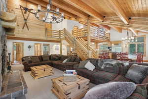 Living room featuring a high ceiling, ceiling fan with notable chandelier, carpet floors, beamed ceiling, and wooden ceiling