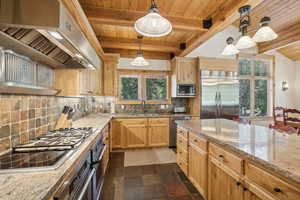 Kitchen featuring tasteful backsplash, built in appliances, beam ceiling, custom range hood, and dark tile patterned flooring