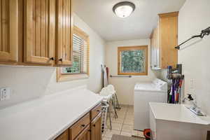 Clothes washing area with sink, cabinets, washing machine and dryer, and light tile patterned floors