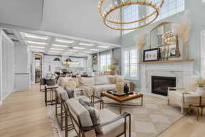 Living room with a fireplace, an inviting chandelier, beam ceiling, coffered ceiling, and light hardwood / wood-style flooring