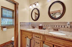 Bathroom with double vanity, toilet, tile patterned floors, and tasteful backsplash