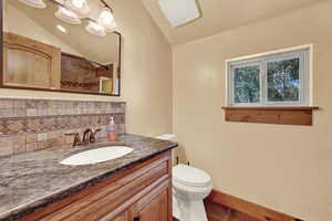 Bathroom with tasteful backsplash, lofted ceiling, tile patterned floors, toilet, and vanity