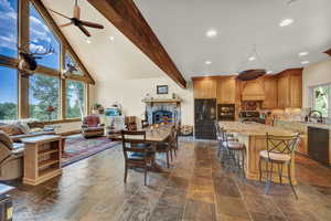 Interior space featuring black appliances, backsplash, a kitchen island with sink, beam ceiling, and ceiling fan