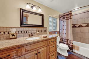 Full bathroom with vanity, tile patterned floors, shower / bath combo with shower curtain, toilet, and backsplash