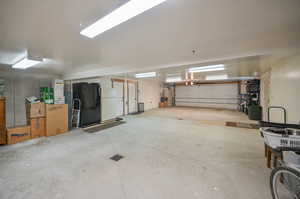 Garage with black refrigerator with ice dispenser and white fridge