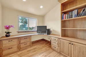 Office featuring light hardwood / wood-style flooring, built in desk, and vaulted ceiling