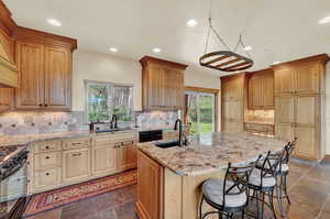 Kitchen featuring dark tile patterned flooring, sink, gas range oven, backsplash, and a kitchen island with sink