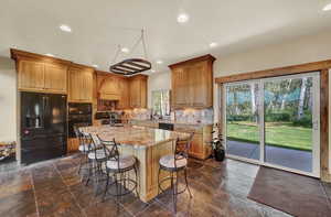 Kitchen featuring decorative backsplash, a kitchen island with sink, black appliances, and a healthy amount of sunlight