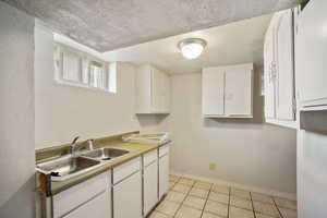 Basement Kitchen featuring sink, white cabinetry, a textured ceiling, and light tile patterned floors