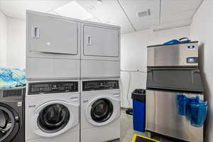 Clothes washing area featuring stacked washer and clothes dryer and light tile patterned floors