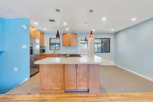 Kitchen with appliances with stainless steel finishes, sink, pendant lighting, light tile patterned floors, and a center island