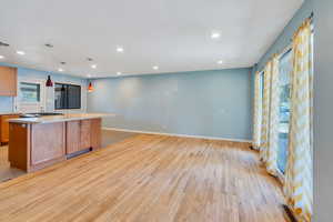 Kitchen with light wood-type flooring, a kitchen island, hanging light fixtures, stainless steel gas stovetop, and light stone counters