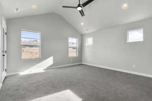 Carpeted spare room featuring vaulted ceiling and ceiling fan