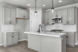 Kitchen featuring gray cabinetry, stove, a kitchen island with sink, sink, and hanging light fixtures