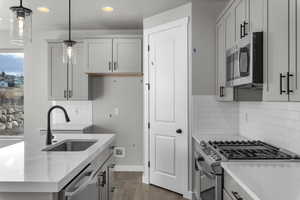 Kitchen with sink, dark wood-type flooring, hanging light fixtures, decorative backsplash, and appliances with stainless steel finishes